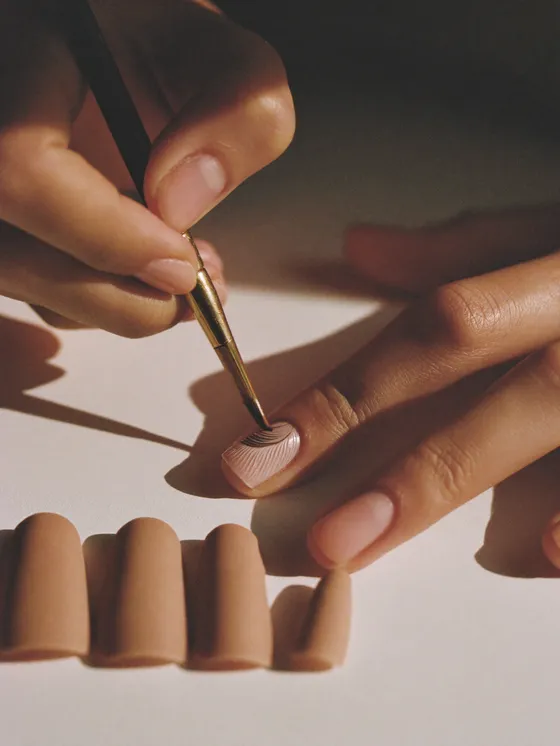 An artist painting a fine hairline graphic onto a single nail